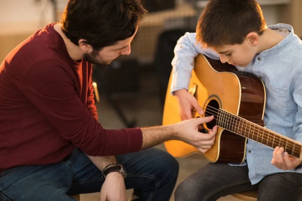A guitar student practicing chords while an instructor demonstrates proper hand placement during a lesson